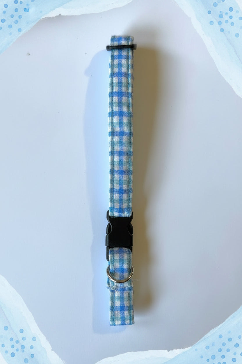 Blue checkered dog collar with a black release buckle and silver d ring on a white background